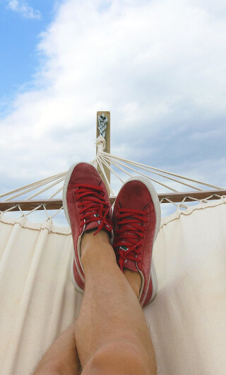 Close up of a man's red shoes in a hammock with a blue cloudy sky in the background