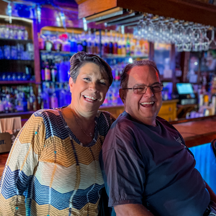 Sheryl and Tony Sylvester smiling while sitting at their bar, Tony's.