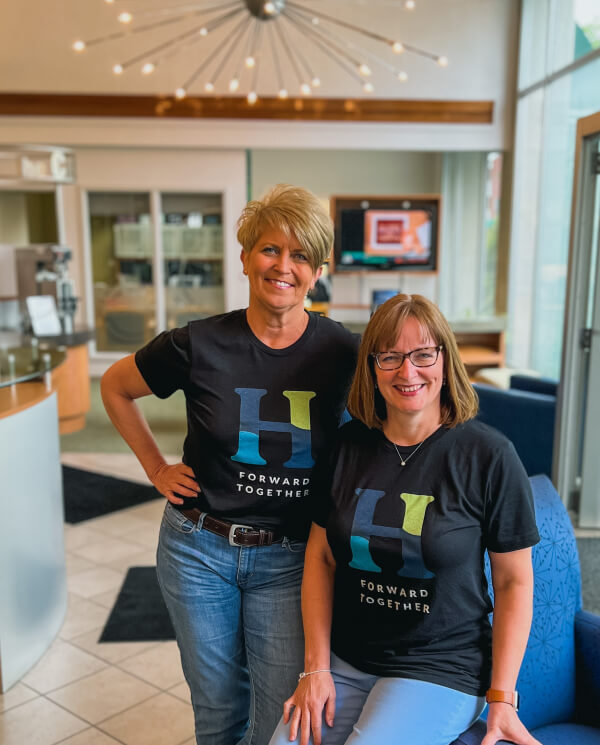 Tammy Bobo and Polly Sumney smiling in Forward Together T-shirts in the Hocking Valley Bank lobby.