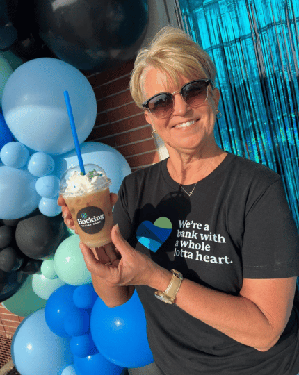 CEO Tammy Bobo smiling and holding an iced "sputnik" coffee at the bank's 60th anniversary.