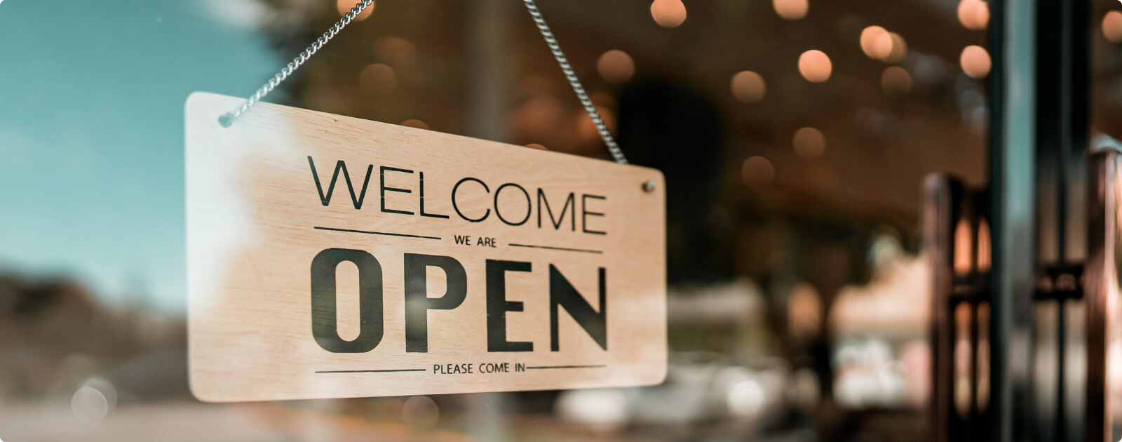 A sign hanging in a window that reads "Welcome, we are open. Please come in."