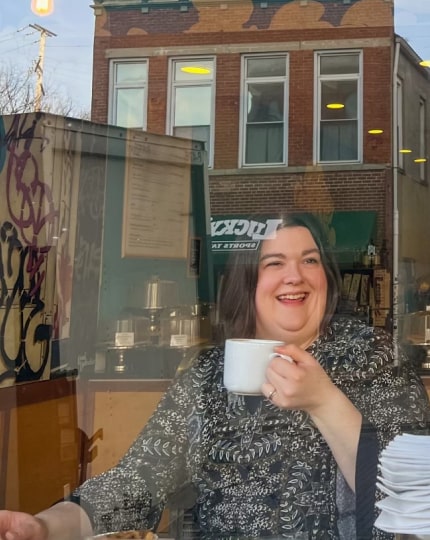 Sarah Greene smiling with a cup of coffee at Fluff Bakery